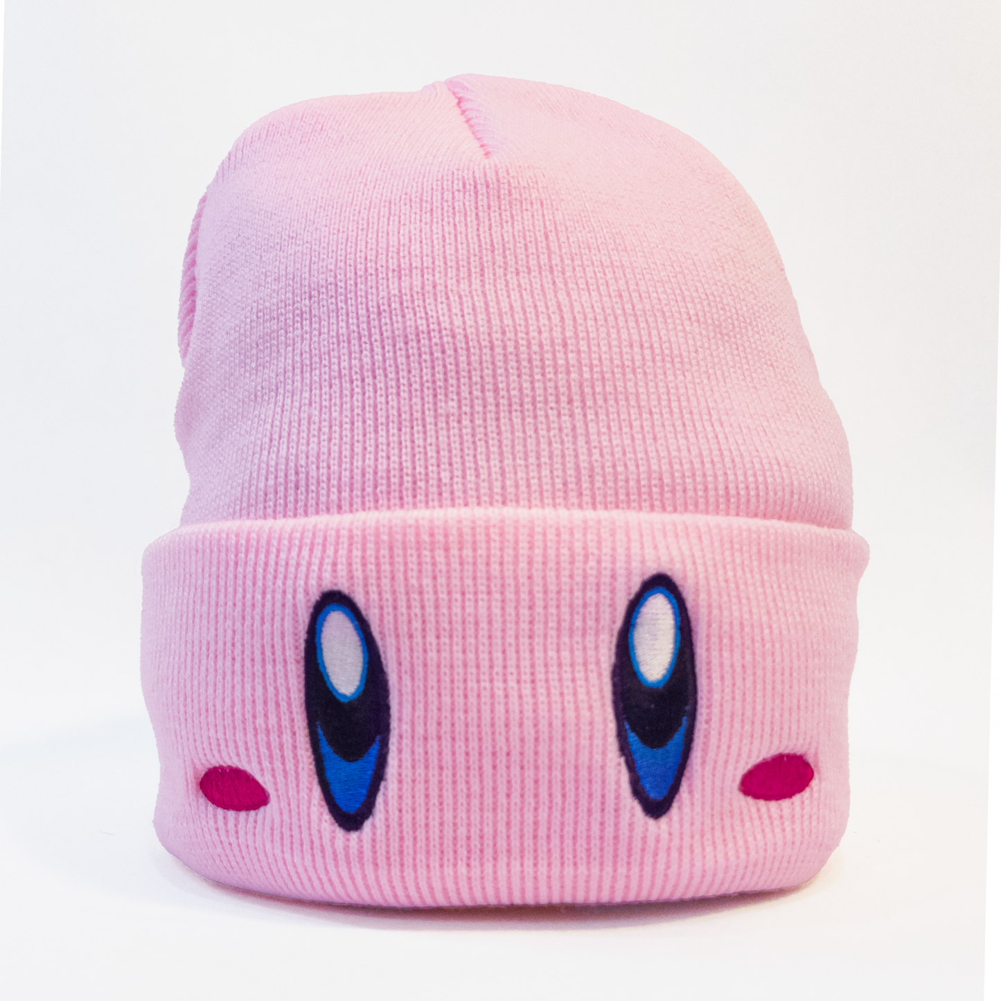 A pink knit hat featuring the face of Kirby, a popular video game character. The hat has Kirby's large blue eyes and small pink cheeks embroidered on the front.