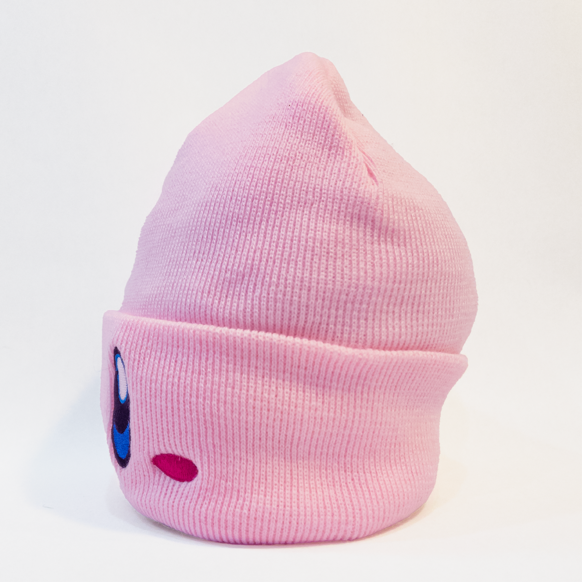 A pink knit hat featuring the face of Kirby, a popular video game character. The hat has Kirby's large blue eyes and small pink cheeks embroidered on the front.